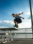 Young man jumping backwards from picnic table on lake pier