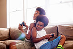 Two brothers back to back whilst playing game controllers in living room