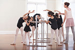 Ballet teacher teaching group of girls ballet position at the barre