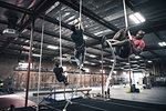 Male and female crossfitters climbing ropes in gym