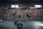 Young male and female crossfitter swinging on gym rings in gym