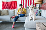 Portrait of young woman using smartphone and cute dog on living room sofa