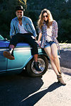 Portrait of couple sitting and leaning against vintage car
