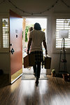 Rear view of young couple carrying suitcases out of front door