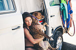 Woman sitting in camper van hugging pet dog