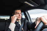 Young businessman driving whilst talking on smartphone