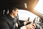 Young businessman driving whilst texting on smartphone