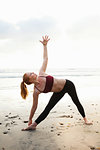 Mid adult woman practicing triangle yoga pose on beach