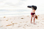 Mid adult woman upside down in yoga position on beach