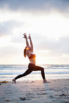 Mid adult woman practicing warrior yoga pose on beach at sunset
