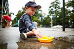 Boy playing with toy boat on water on pavement
