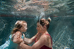 Underwater shot of mother holding daughter and helping her to learn to swim