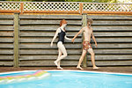 Young couple wearing swimwear holding hands on poolside