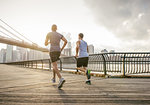 Rear view of two male running friends running in front of Brooklyn bridge, New York, USA