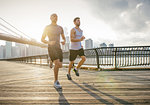 Two male running friends running in front of Brooklyn bridge, New York, USA