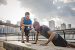 Personal trainer and young man doing push ups on riverside bench, Brooklyn, New York, USA