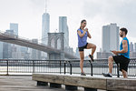 Personal trainer and young woman balancing on riverside bench, Brooklyn, New York, USA
