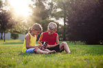 Brother and sister sitting on grass looking down stroking Boston Terrier puppy