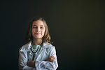 Portrait of girl dressed up as doctor wearing stethoscope, arms crossed looking away smiling