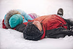 Father and daughter wearing knit hats lying on backs in snow