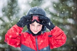Boy wearing helmet and skiing goggles looking at camera smiling, snowing
