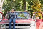 Portrait of boy sitting on hood of pickup truck in woods