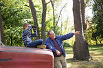 Senior and grandson pointing and using binoculars in woods