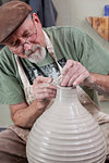 Potter wearing flat cap finishing shaping clay vase, looking down