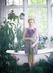 Young woman holding bouquet of flowers, standing in bathroom filled with plants