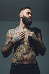 Portrait of  young man with beard, bare chest covered in tattoos