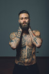 Portrait of  young man with beard, bare chest covered in tattoos, hands behind neck
