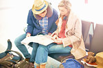 Young couple sitting in airport departure lounge, looking at map, planning trip