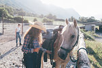 Young cowgirl checking saddle in rural equestrian arena