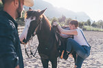 Young woman mounting horse in rural equestrian arena