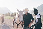 Cowboy handing horse's reins to young man in rural equestrian arena, Primaluna, Trentino-Alto Adige, Italy