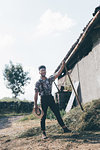 Young male agricultural worker with pitchfork, full length portrait