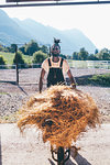 Cool young man with wheelbarrow hay in rural equestrian arena, portrait