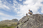 Boy and father crouching on top of rock formation, low angle view, Oppland, Nord-Trondelag, Norway