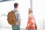 Young couple at airport, carrying backpacks, looking out of window