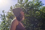 Young woman in knitted hat contemplating in front of tree foliage, backlit head and shoulder profile