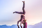 Two young women practicing acroyoga in front of mountain range at sunset, Squamish, British Columbia, Canada