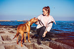 Stylish mid adult woman crouching on sea defence petting her dog, Odessa, Odeska Oblast, Ukraine