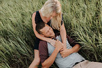 Romantic young woman and boyfriend reclining together in field of long grass