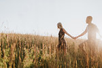 Romantic man and girlfriend holding hands in field of sunlit long grass