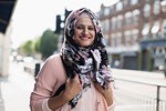 Portrait smiling, young woman wearing floral hijab on urban sidewalk