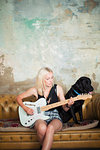 Young woman with dog playing electric guitar on sofa