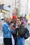 Young women friends using digital camera on urban street
