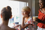 Young women friends drinking coffee at apartment window