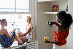 Young woman with camera phone photographing friends sitting in apartment window