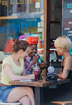 Young women friends drinking smoothies and eating at sidewalk cafe